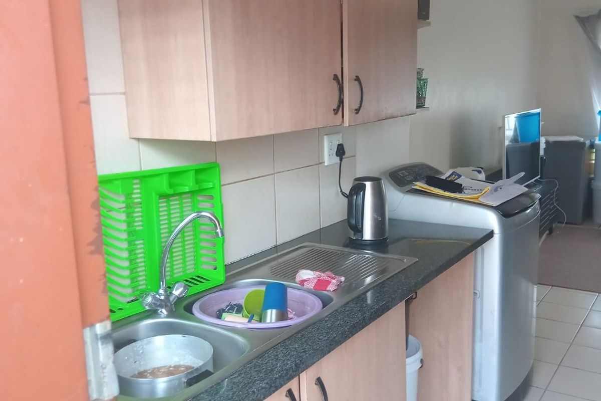 A functional kitchen area featuring laminate cabinetry, a double bowl sink with mixer tap, tiled splashback, and ceramic floor tiles.