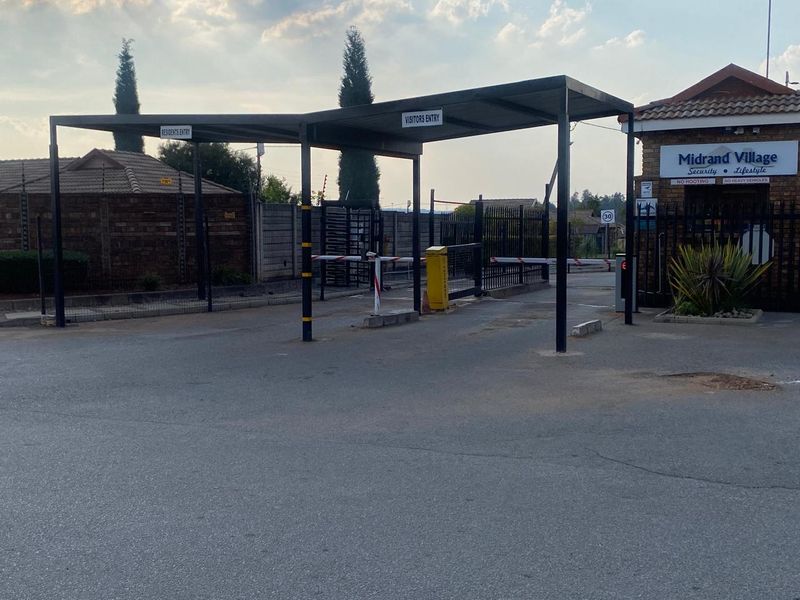 The entrance to Midrand Village featuring a secure boom gate system, covered access points, and brick boundary walls with integrated security fencing.