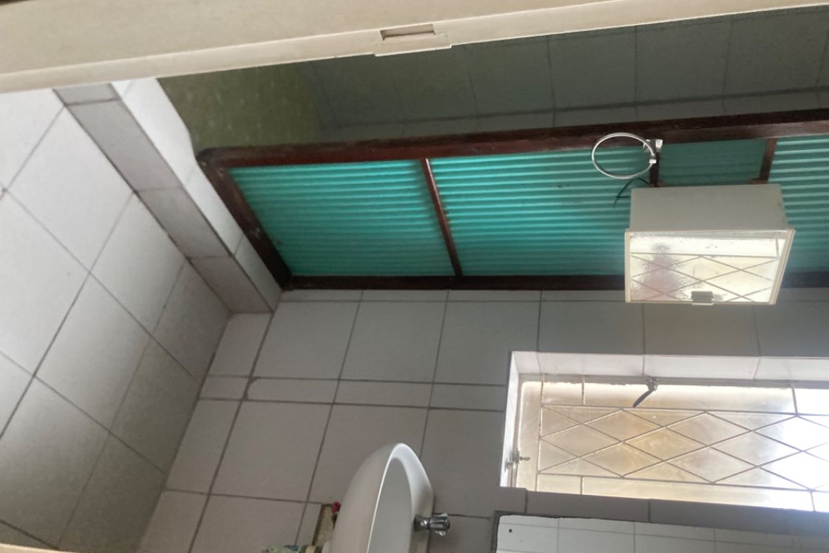 A compact bathroom featuring tiled walls and flooring, a pedestal basin, and a window with security bars, requiring cosmetic updates.