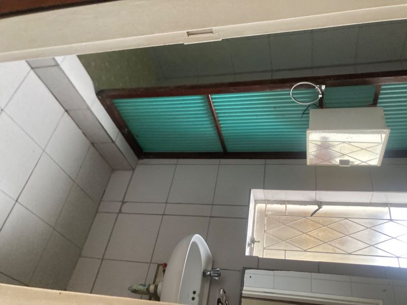 A compact bathroom featuring tiled walls and flooring, a pedestal basin, and a window with security bars, requiring cosmetic updates.