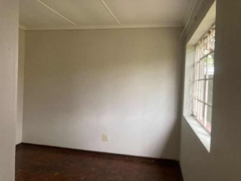 An empty bedroom featuring original wooden parquet flooring, a steel-framed window, and coved ceiling details, ready for renovation or staging.
