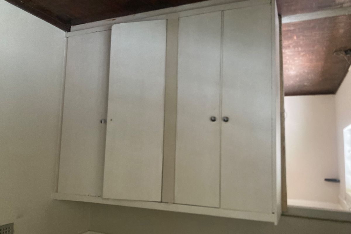 A bedroom interior featuring built-in white cupboards and a dark timber ceiling, requiring cosmetic updates to improve the overall aesthetic.