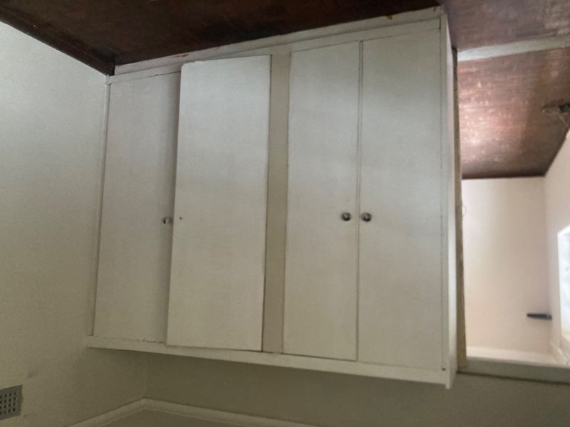 A bedroom interior featuring built-in white cupboards and a dark timber ceiling, requiring cosmetic updates to improve the overall aesthetic.