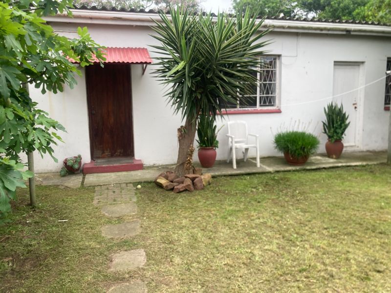 Rear exterior view of the apartment featuring a small garden area, concrete pathway, and a covered entrance with a timber door.