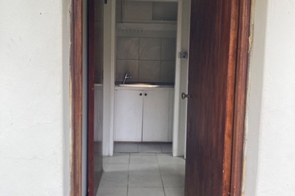 A functional scullery or utility area featuring built-in cabinetry, a stainless steel sink, and tiled flooring, accessible through a wooden doorway.