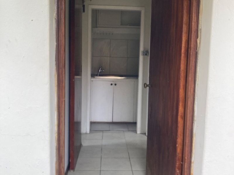 A functional scullery or utility area featuring built-in cabinetry, a stainless steel sink, and tiled flooring, accessible through a wooden doorway.