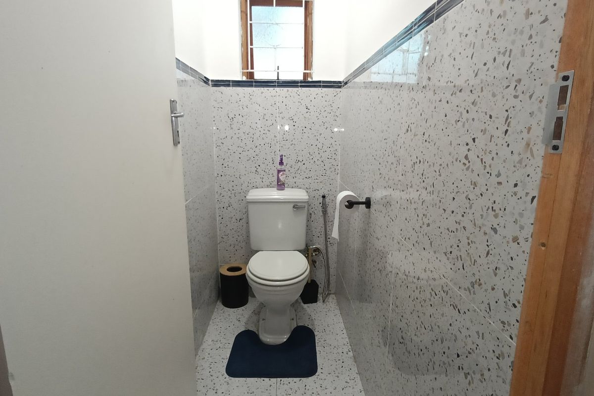 A compact bathroom featuring terrazzo-style wall and floor tiling, equipped with a standard toilet and bidet spray.