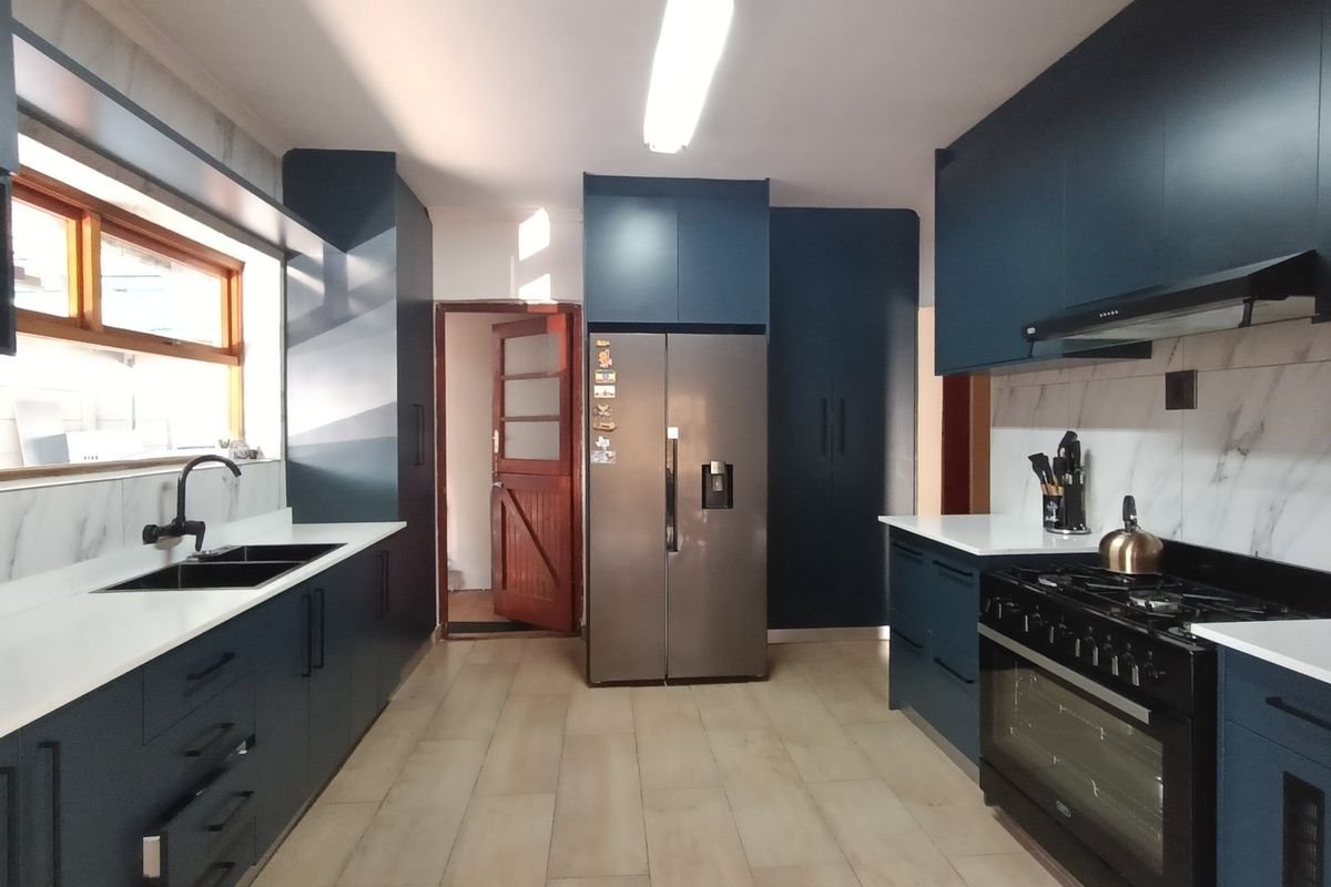 Modern kitchen featuring dark blue cabinetry, white stone countertops, marble-look splashbacks, gas stove with extractor, and tiled flooring.