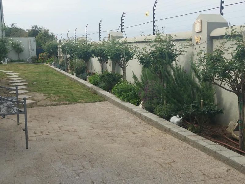 A well-maintained rear garden featuring a paved patio area, established landscaping, and a secure perimeter wall with electric fencing.