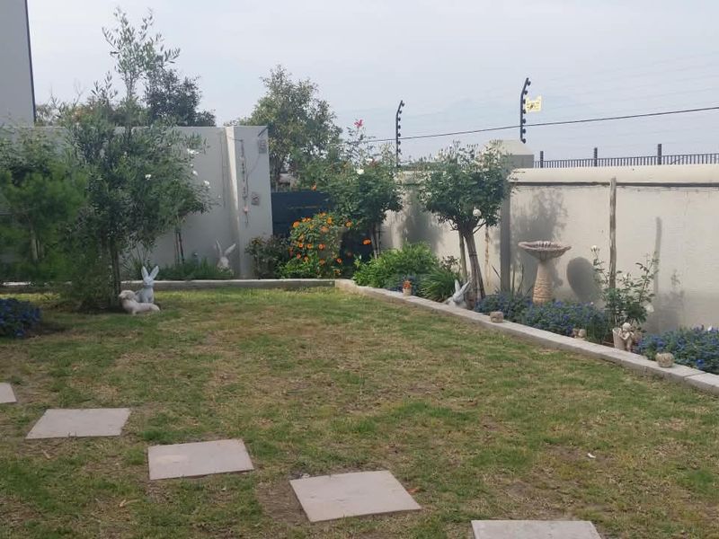 A well-maintained private garden featuring a lawn, paved stepping stones, established trees, and a secure perimeter wall with electric fencing.