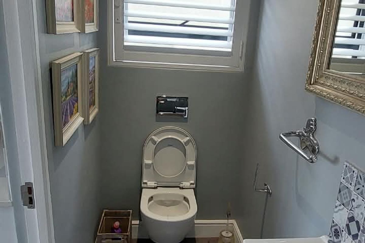 A well-maintained guest bathroom featuring a wall-mounted toilet, modern vanity with basin, and neutral grey wall tones.