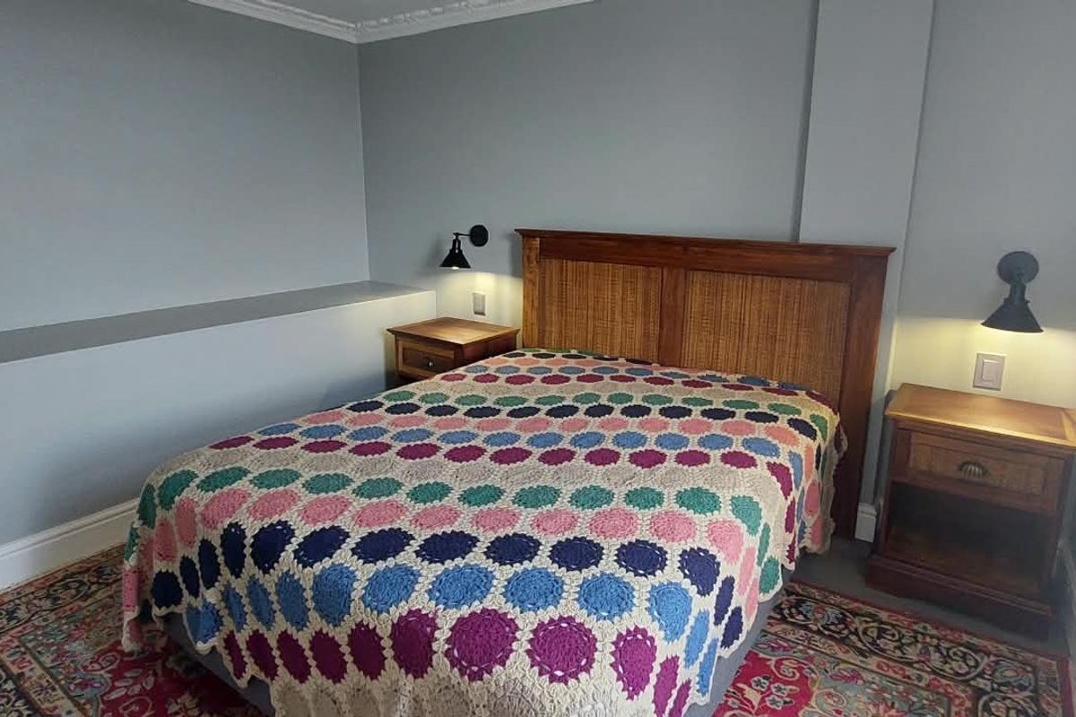 A well-maintained bedroom featuring crown molding, plantation shutters, and wall-mounted reading lights, providing a comfortable and functional sleeping space.