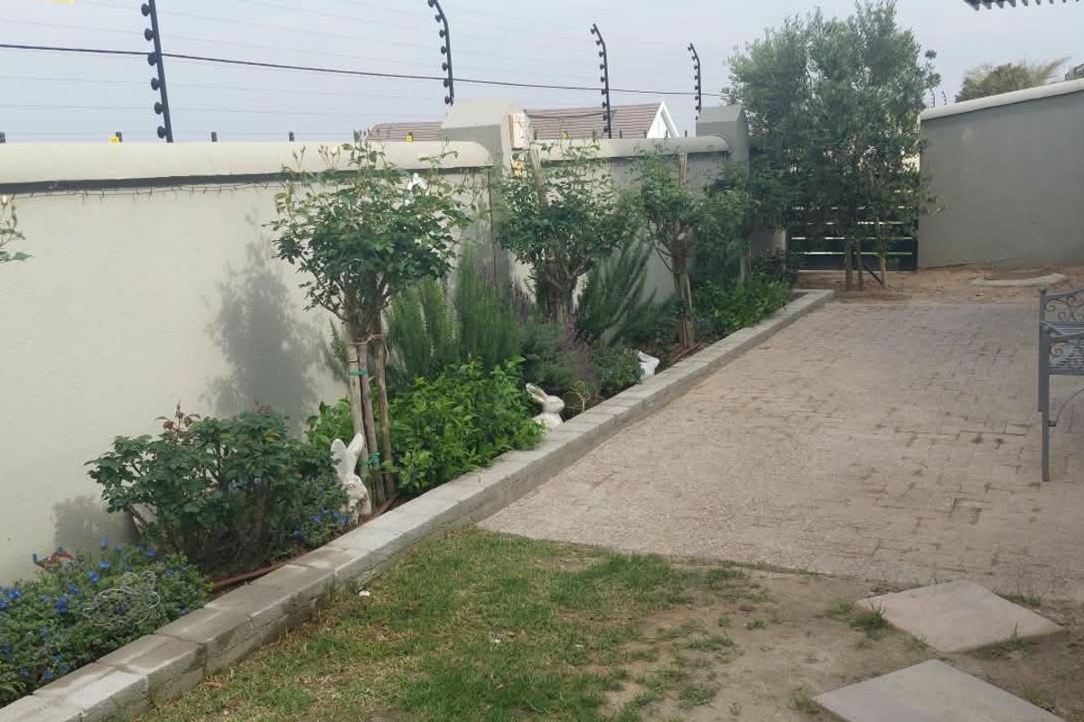 A private rear courtyard featuring a paved patio area, landscaped garden beds, and secure perimeter walling with electric fencing.