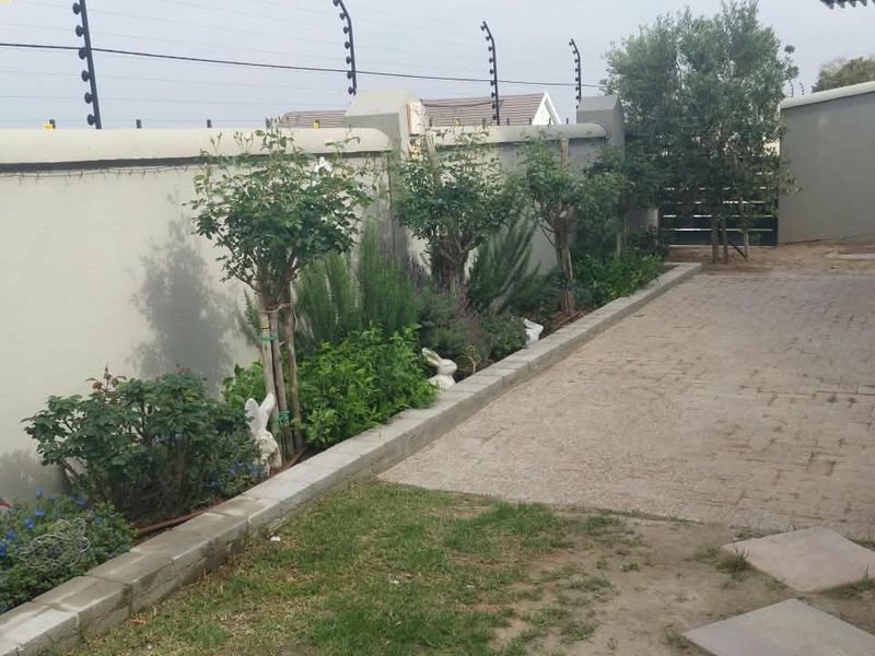 A private rear courtyard featuring a paved patio area, landscaped garden beds, and secure perimeter walling with electric fencing.