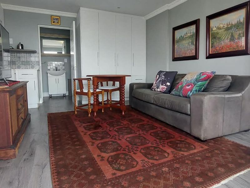 Open-plan living area featuring laminate flooring, built-in storage cupboards, and crown molding, with an adjacent bathroom visible in the background.