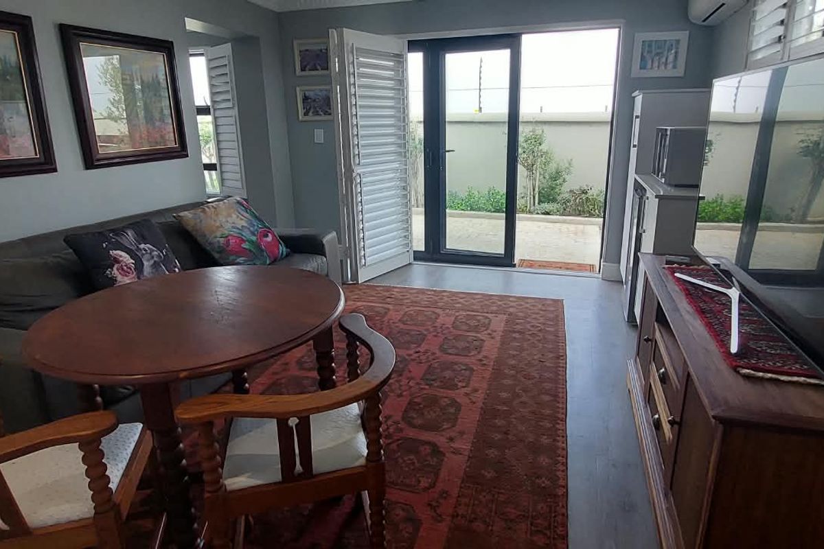 A comfortable living room featuring laminate flooring, air conditioning, and direct access to an outdoor patio area through sliding glass doors with plantation shutters.
