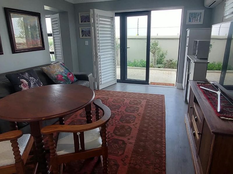 A comfortable living room featuring laminate flooring, air conditioning, and direct access to an outdoor patio area through sliding glass doors with plantation shutters.