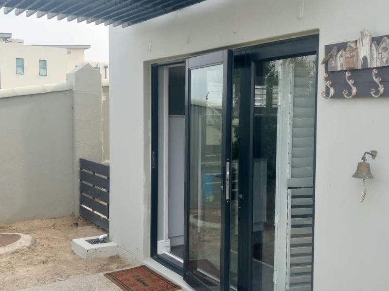 Rear exterior view of the apartment featuring black aluminium sliding doors, a small concrete patio area, and a boundary wall.