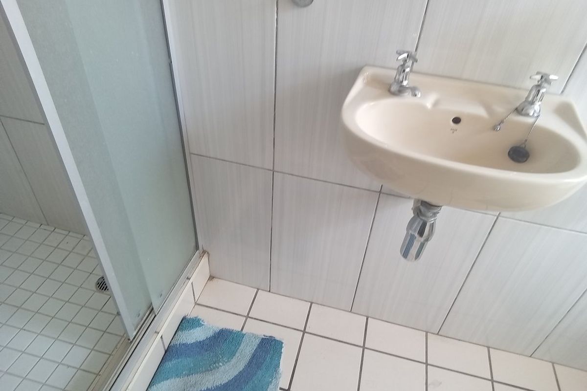 A functional bathroom featuring a wall-mounted basin and a glass-enclosed shower with tiled walls and flooring.