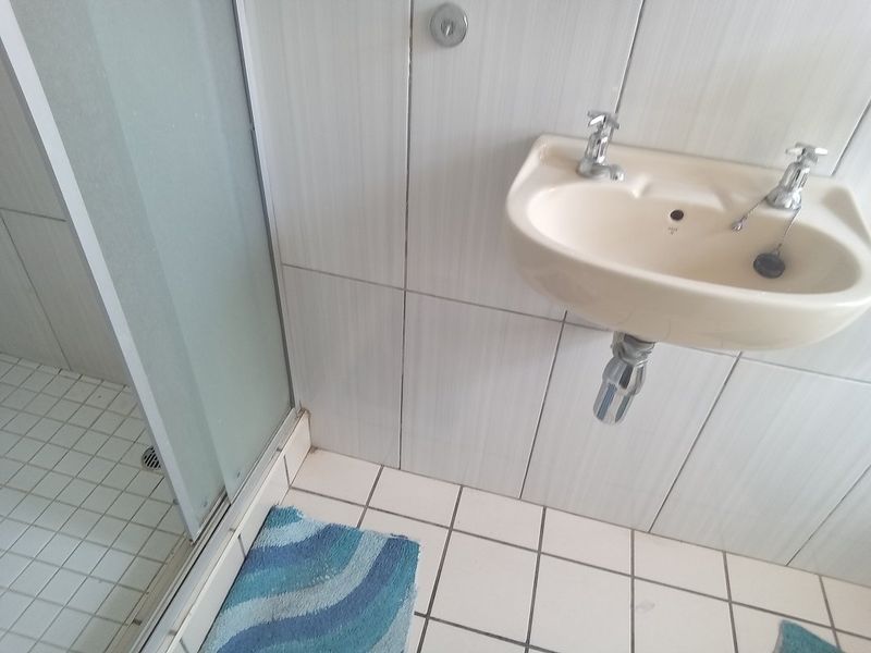 A functional bathroom featuring a wall-mounted basin and a glass-enclosed shower with tiled walls and flooring.