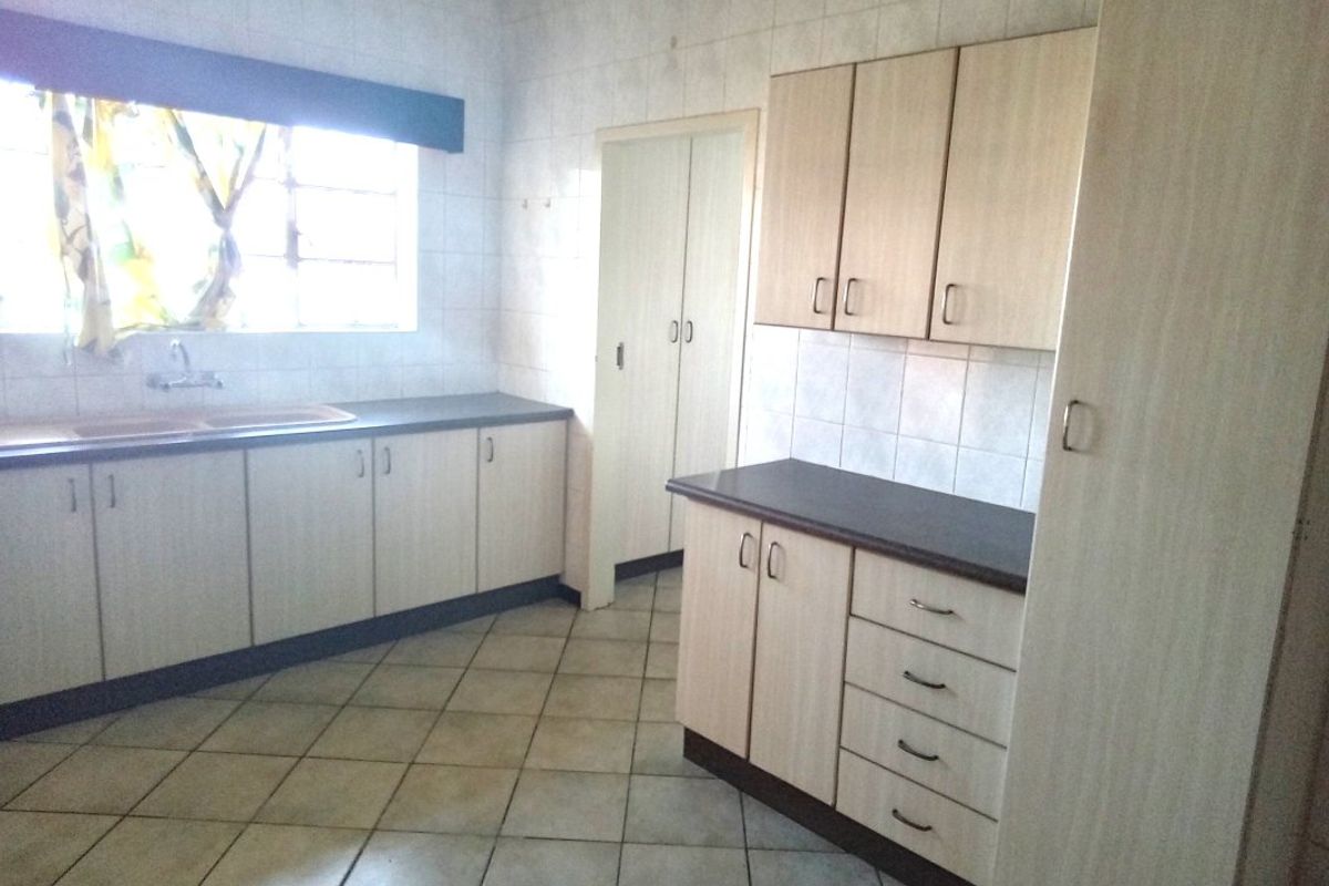 A functional kitchen featuring light-toned laminate cabinetry, dark countertops, tiled flooring, and a built-in pantry cupboard, offering a clean and practical workspace.