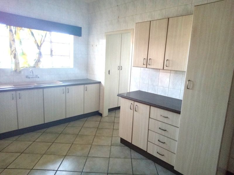 A functional kitchen featuring light-toned laminate cabinetry, dark countertops, tiled flooring, and a built-in pantry cupboard, offering a clean and practical workspace.