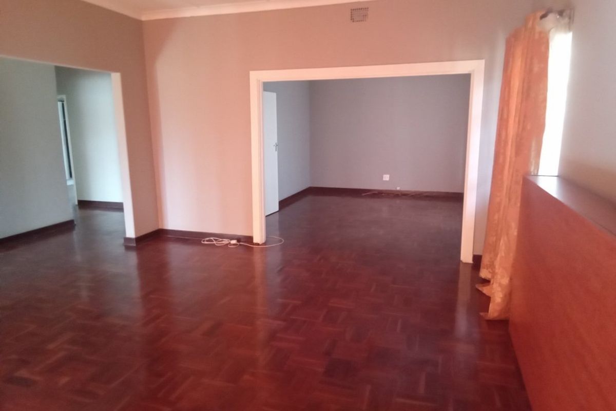 Spacious living area featuring classic parquet flooring and an open-plan layout connecting to adjacent rooms.