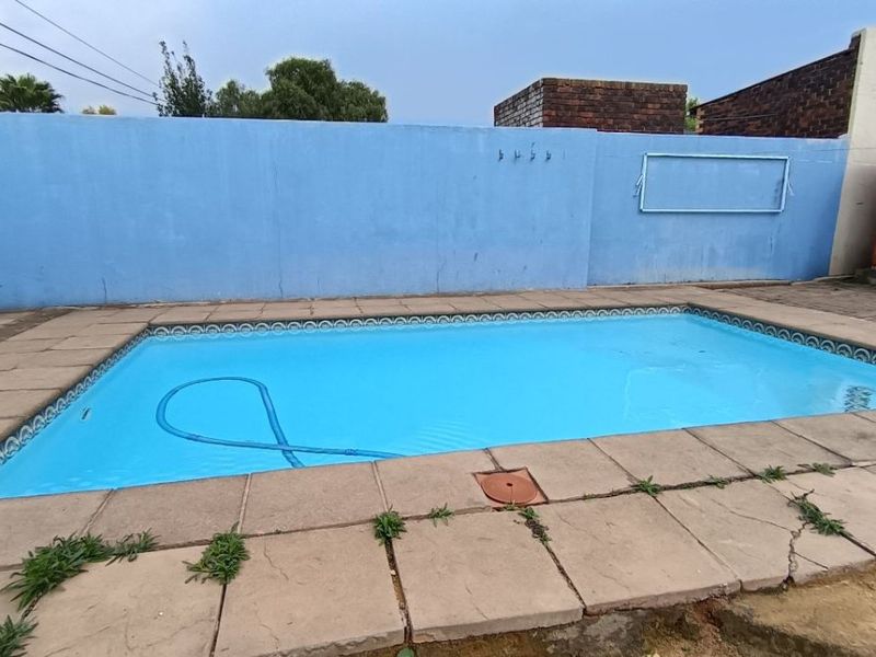 Outdoor swimming pool area featuring paved surround and a high boundary wall, requiring maintenance to the paving and wall finishes.