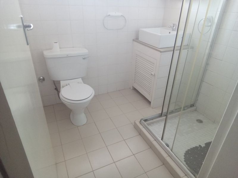 A functional bathroom featuring a white toilet, a vanity cabinet with a vessel sink, and a glass-enclosed shower with tiled finishes.