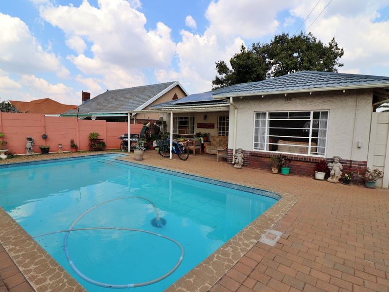 Rear exterior view featuring a swimming pool, paved patio area, and a house with a tiled roof and solar panels.