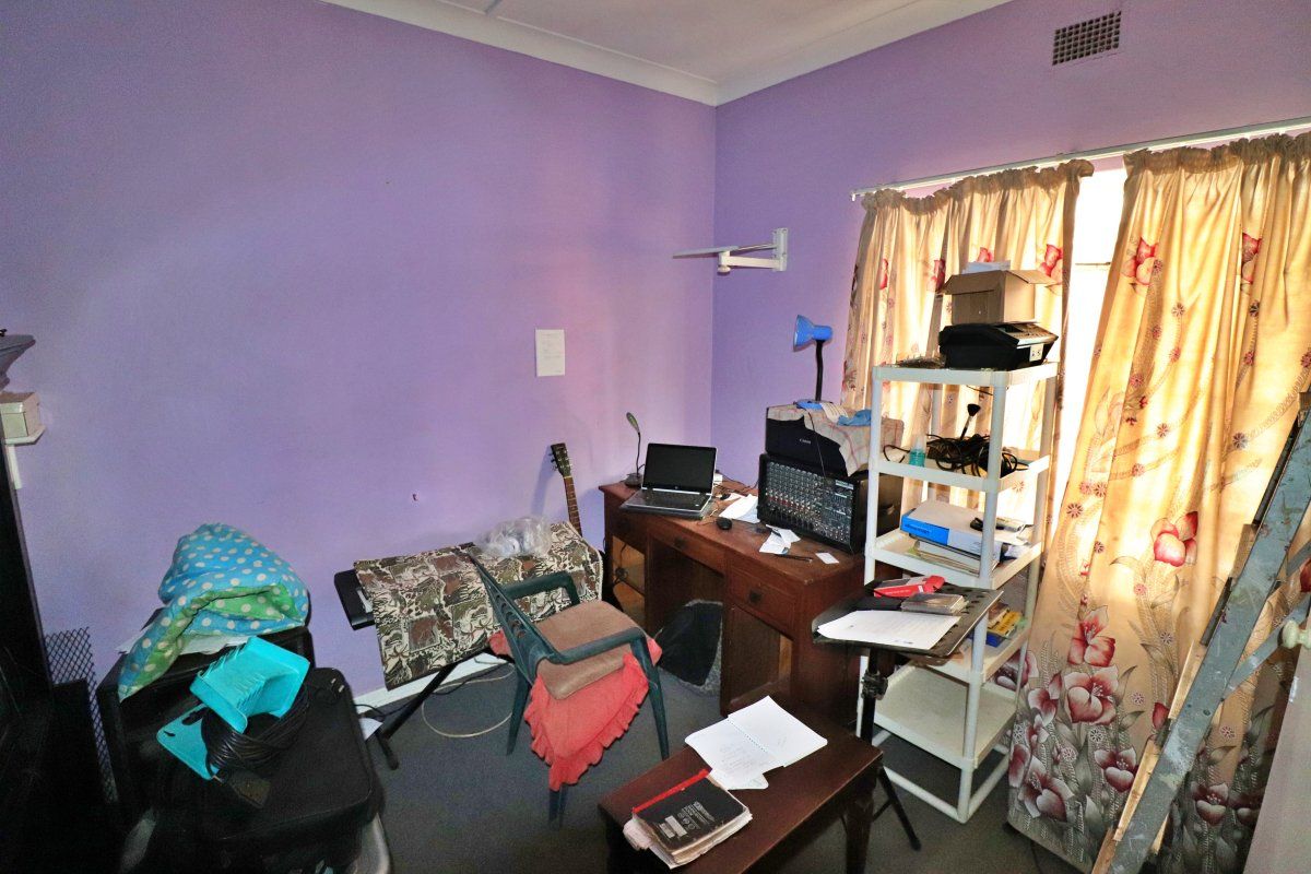 A bedroom space featuring coving and a wall-mounted air vent, currently used as a home office and storage area.
