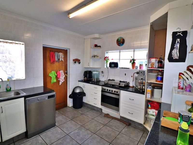 A functional kitchen featuring built-in cabinetry, granite countertops, a gas hob with oven, and tiled finishes throughout.