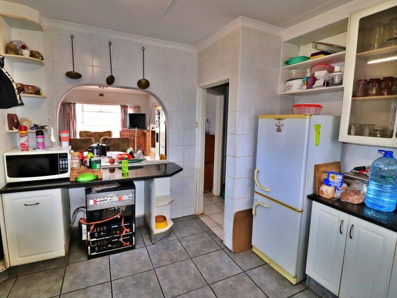 A functional kitchen featuring tiled walls and flooring, granite countertops, and built-in cabinetry with an open archway leading to the living area.