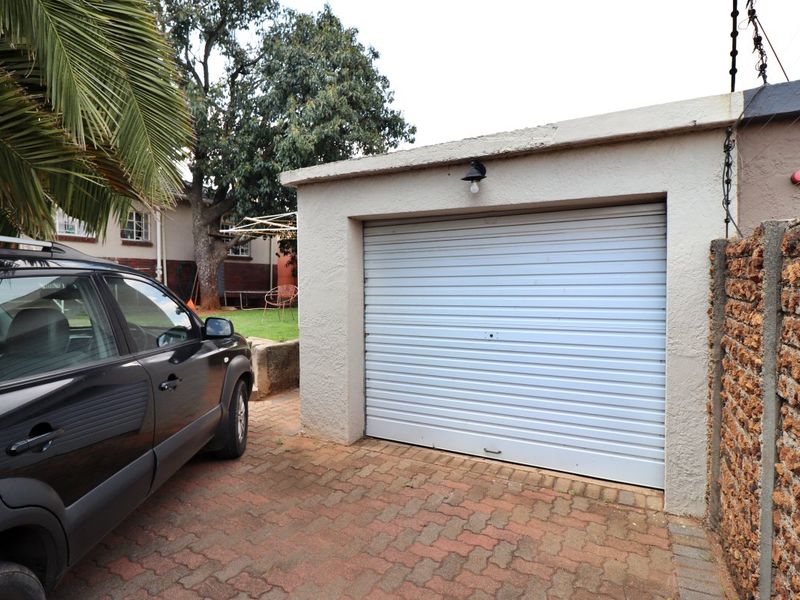 A single garage featuring a roller shutter door, paved driveway, and perimeter electric fencing.