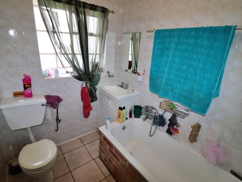 A functional bathroom featuring a bathtub, toilet, and vanity basin with tiled finishes, offering potential for modernization and cosmetic updates.