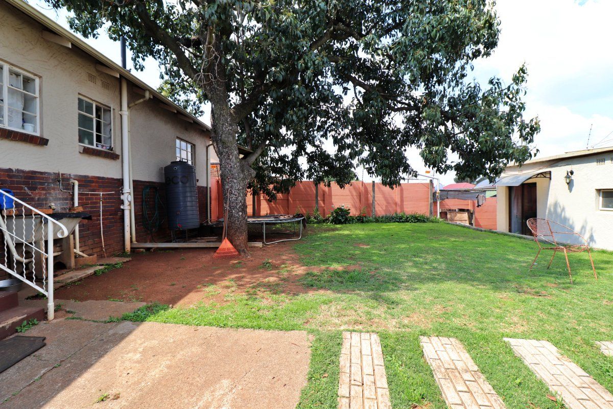 A spacious rear garden featuring a large mature tree, brick boundary walls, a water tank, and a combination of lawn and paved areas.