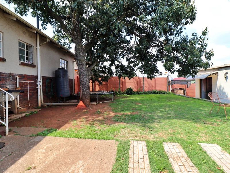 A spacious rear garden featuring a large mature tree, brick boundary walls, a water tank, and a combination of lawn and paved areas.