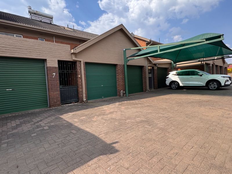 Front exterior view of a townhouse featuring multiple roller shutter garage doors, a paved driveway, and a covered carport area.