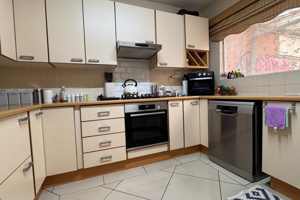 A functional kitchen featuring cream-colored cabinetry, laminate countertops, a gas hob with extractor, built-in oven, and tiled flooring.
