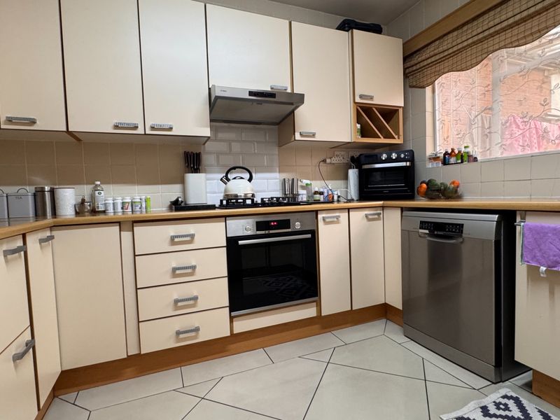 A functional kitchen featuring cream-colored cabinetry, laminate countertops, a gas hob with extractor, built-in oven, and tiled flooring.