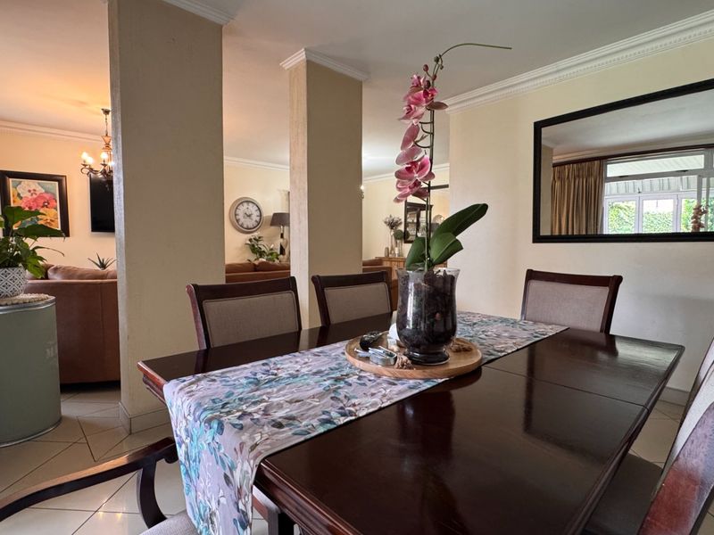 Open plan dining and living area featuring tiled flooring, crown molding, and structural columns, creating a connected and spacious layout.