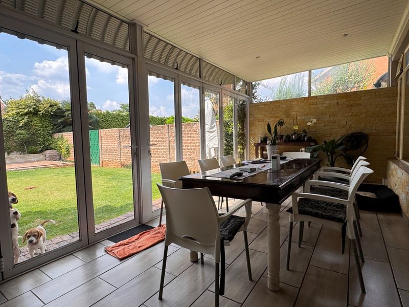 A bright, enclosed patio featuring large stacking glass doors, stone cladding, and tiled flooring, offering a seamless transition to the garden.