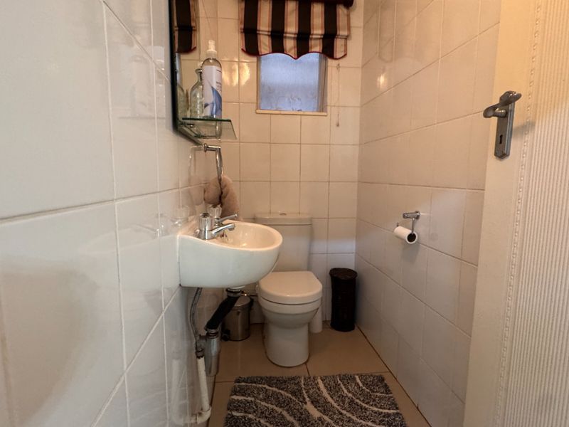 A compact guest bathroom featuring white wall tiles, a wall-mounted basin, and a standard toilet.