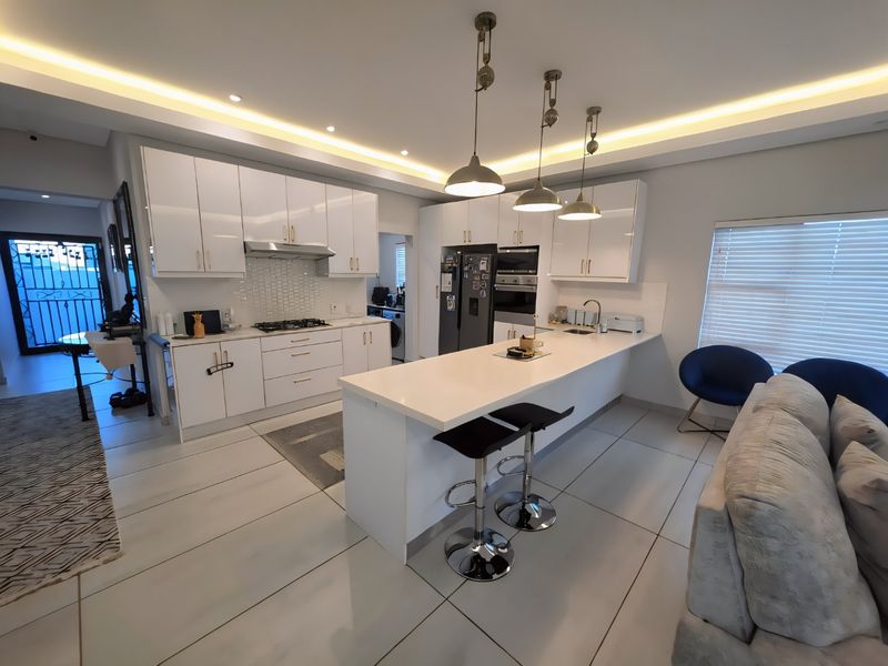 Modern open-plan kitchen featuring high-gloss white cabinetry, a central island with quartz countertops, integrated appliances, and stylish pendant lighting.