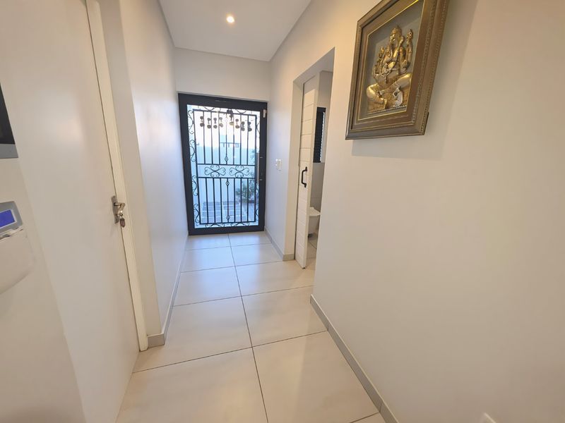 A clean, well-lit hallway featuring neutral floor tiles, recessed lighting, and a secure entrance gate leading to the exterior.