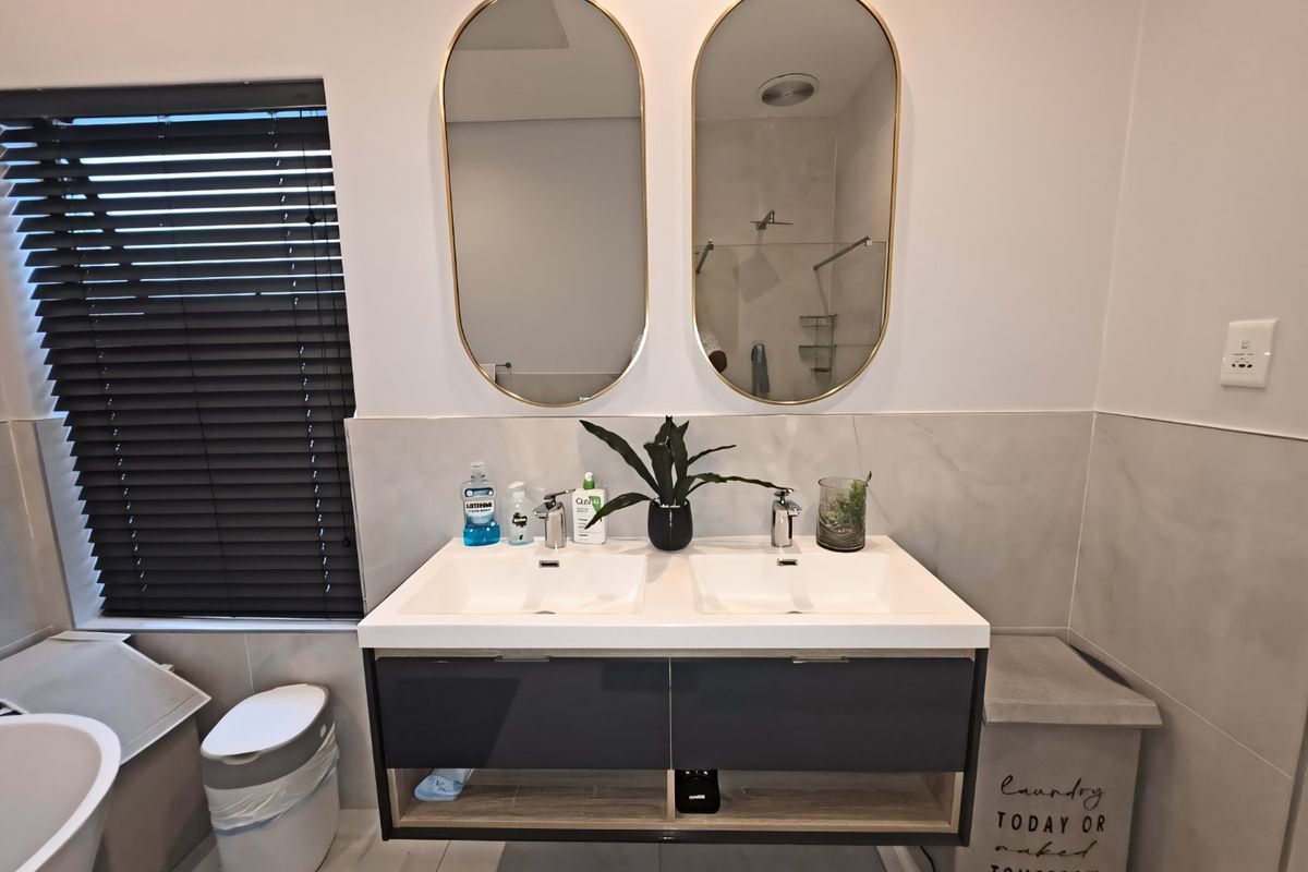 Modern bathroom featuring a sleek wall-mounted double vanity with dual basins, contemporary mixer taps, and stylish oval mirrors against a tiled splashback.