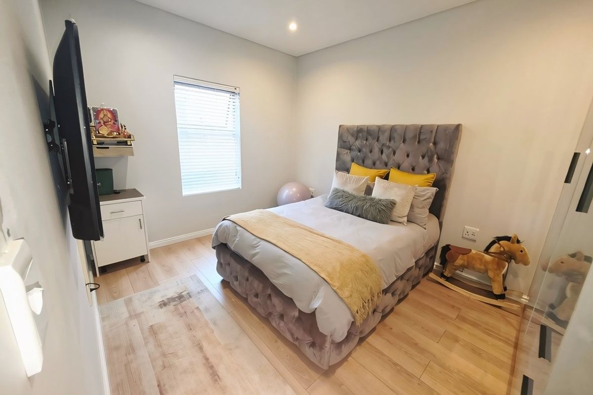A well-maintained bedroom featuring light-toned laminate flooring, recessed downlighting, and a window fitted with venetian blinds.