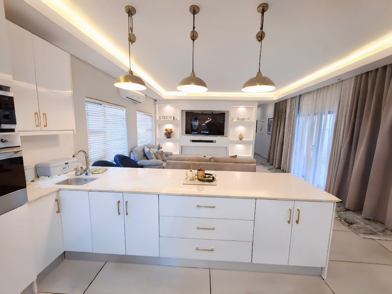 Modern open-plan living area featuring a sleek kitchen with stone island, built-in cabinetry, and a custom media wall with integrated lighting.