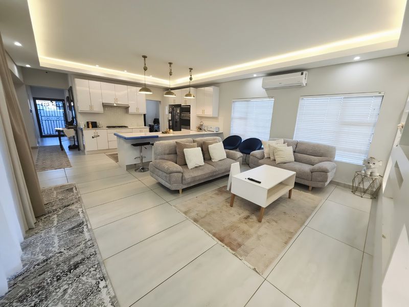 Modern open-plan living area featuring a sleek kitchen with island, recessed ceiling lighting, and tiled floors, creating a bright and cohesive living space.