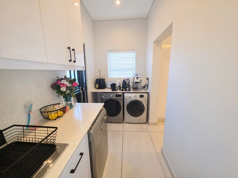 A modern, well-maintained laundry room featuring sleek white cabinetry, stone countertops, tiled flooring, and dedicated space for laundry appliances.
